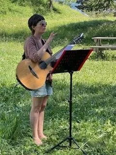 Lysiane Cueff, guitare en bandoulière devant un pupitre, mène un chant dans un pré