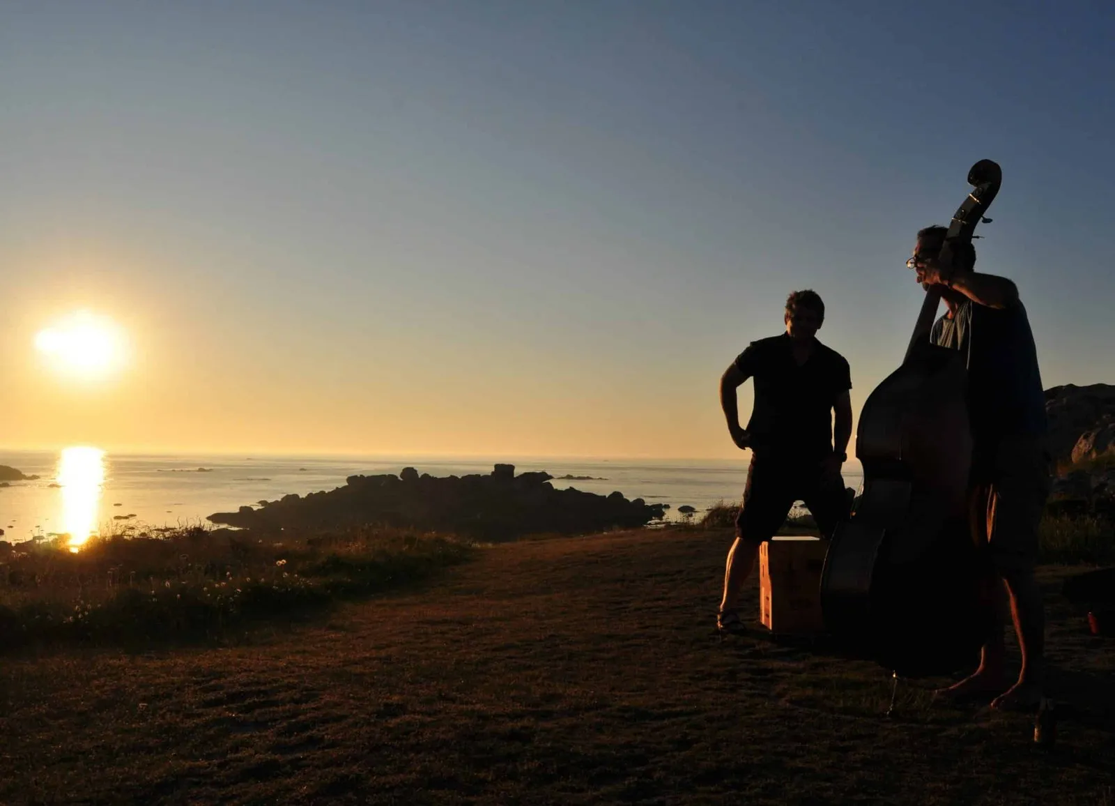 Deux silhouettes et une contrebasse face au soleil couchant sur la mer
