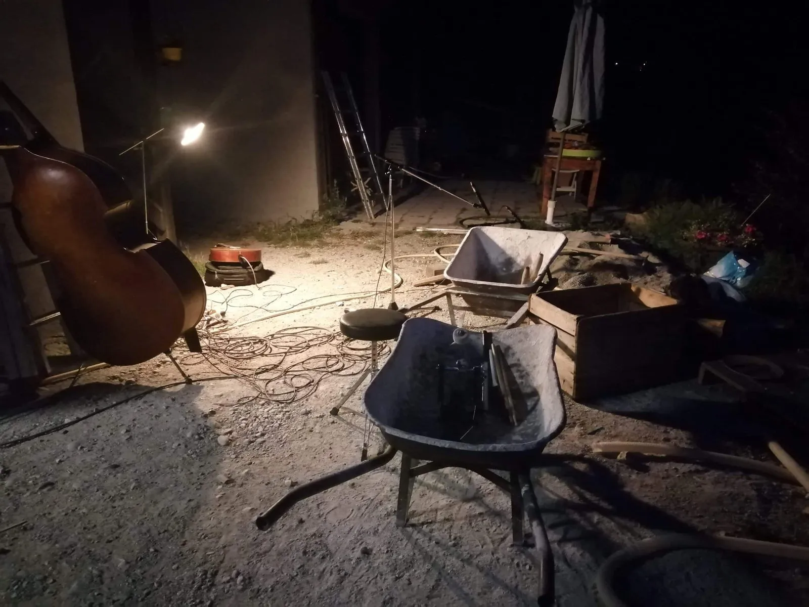 Une contrebasse, des micros et une brouette éclairés de nuit, en extérieur
