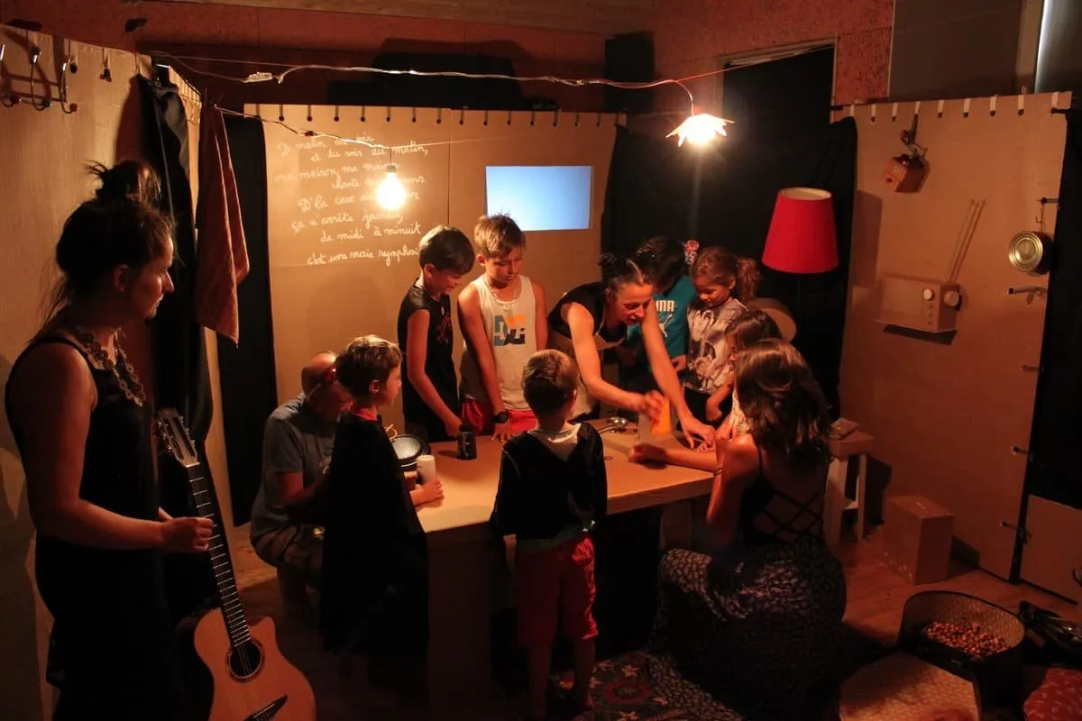 Les comédiennes et les enfants réunis autour d’une table, dans le décor en carton