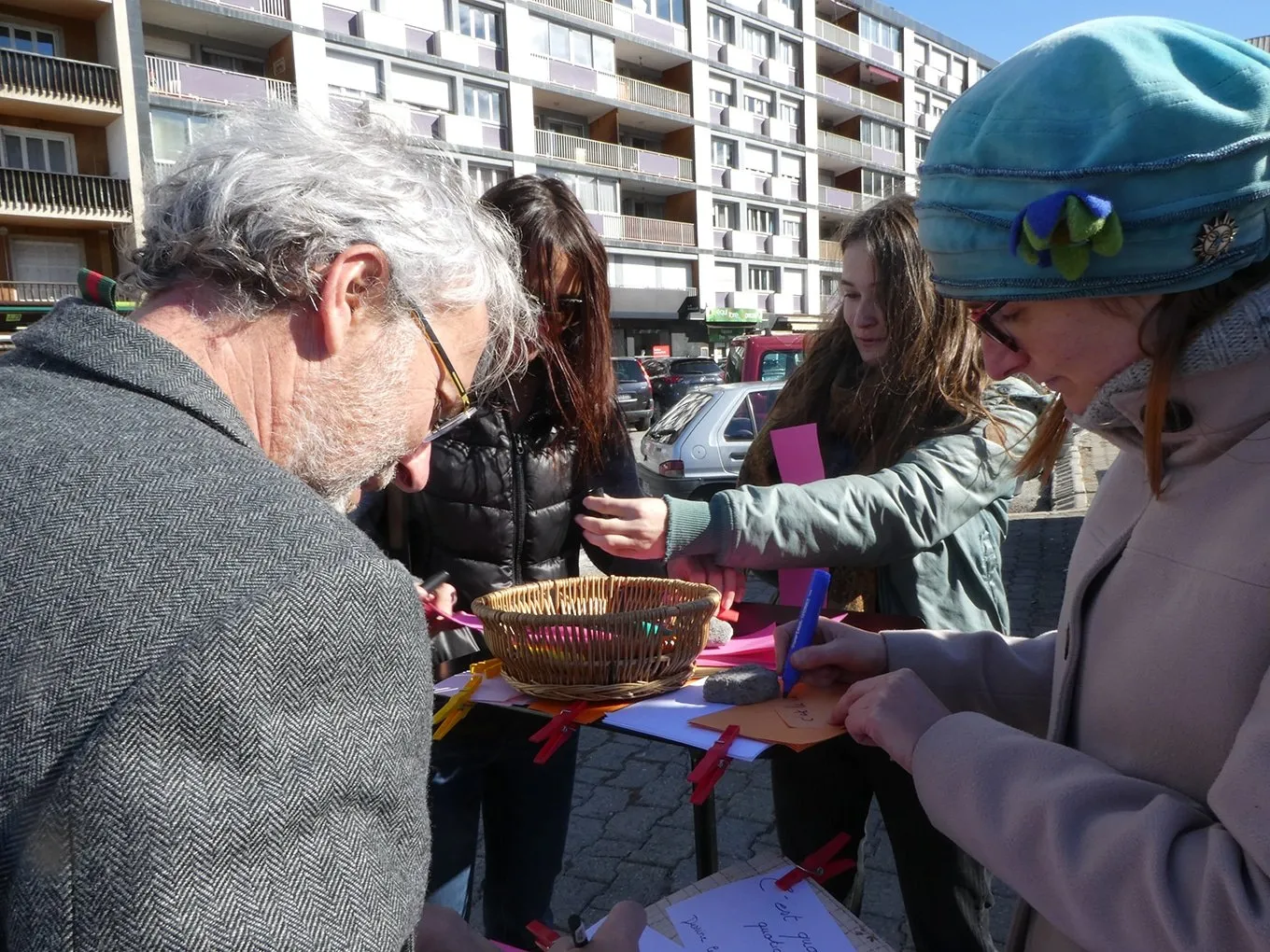 Des passants écrivent sur des papiers de couleur lors d’une animation de rue